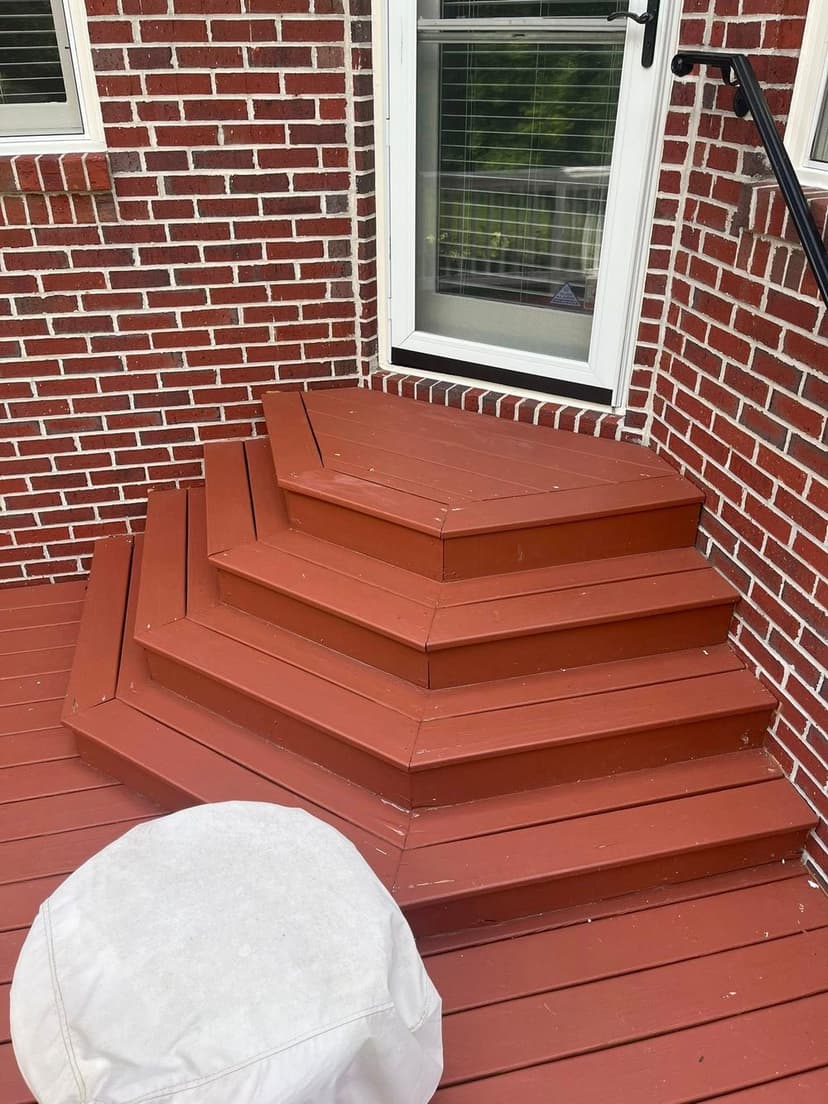 Red painted wooden steps leading to a door on a brick home exterior.